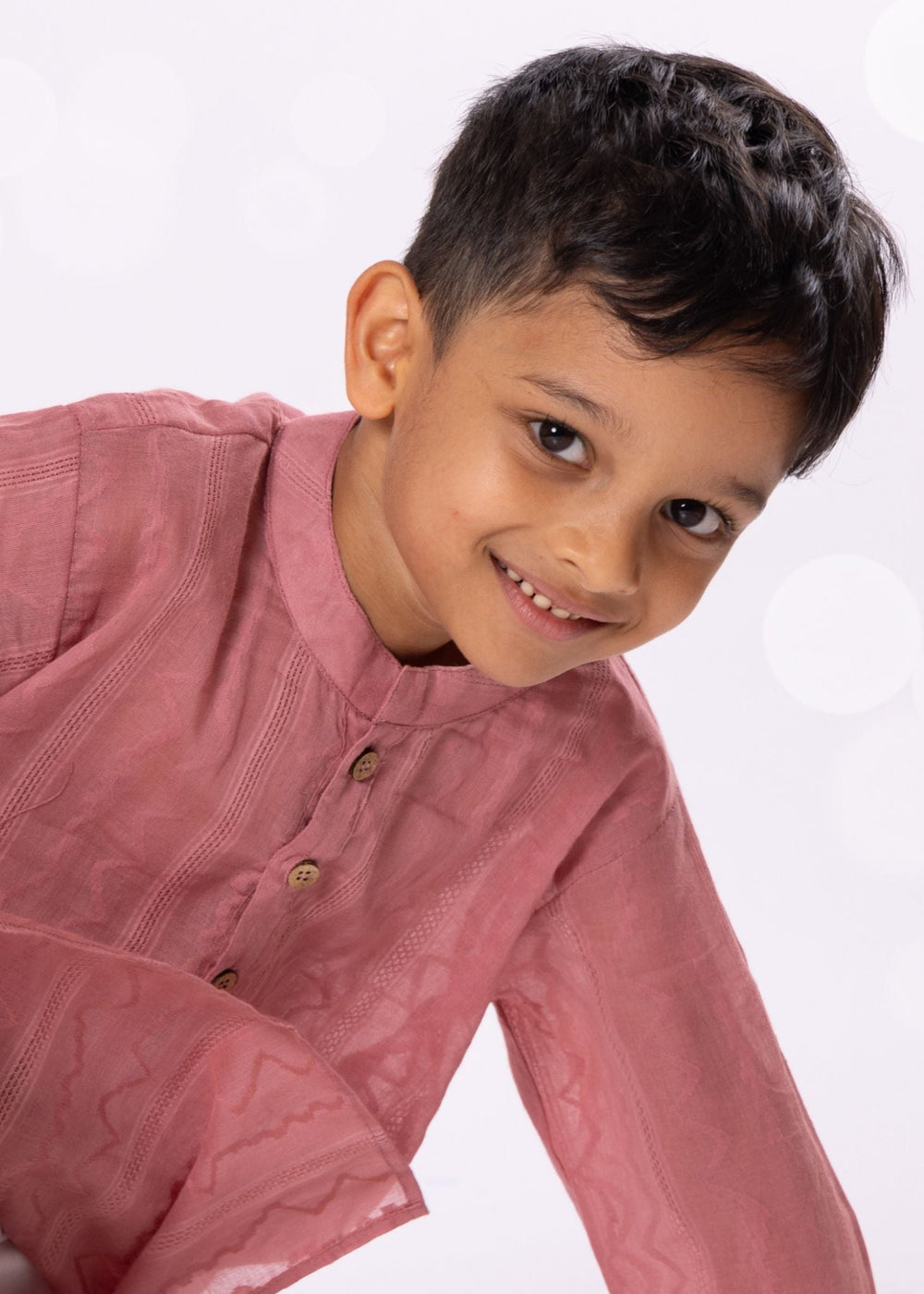 Young boy wearing a pink traditional outfit on a white background