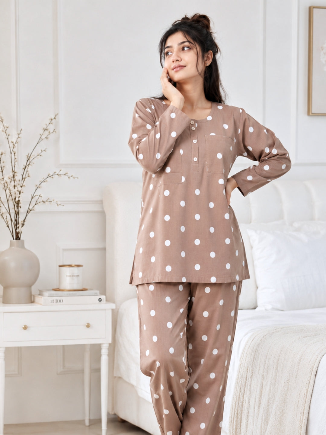 Woman standing in a bedroom in a Tura Turi mocha polka dot cotton night suit, showing the tunic-length top and full-length pyjama