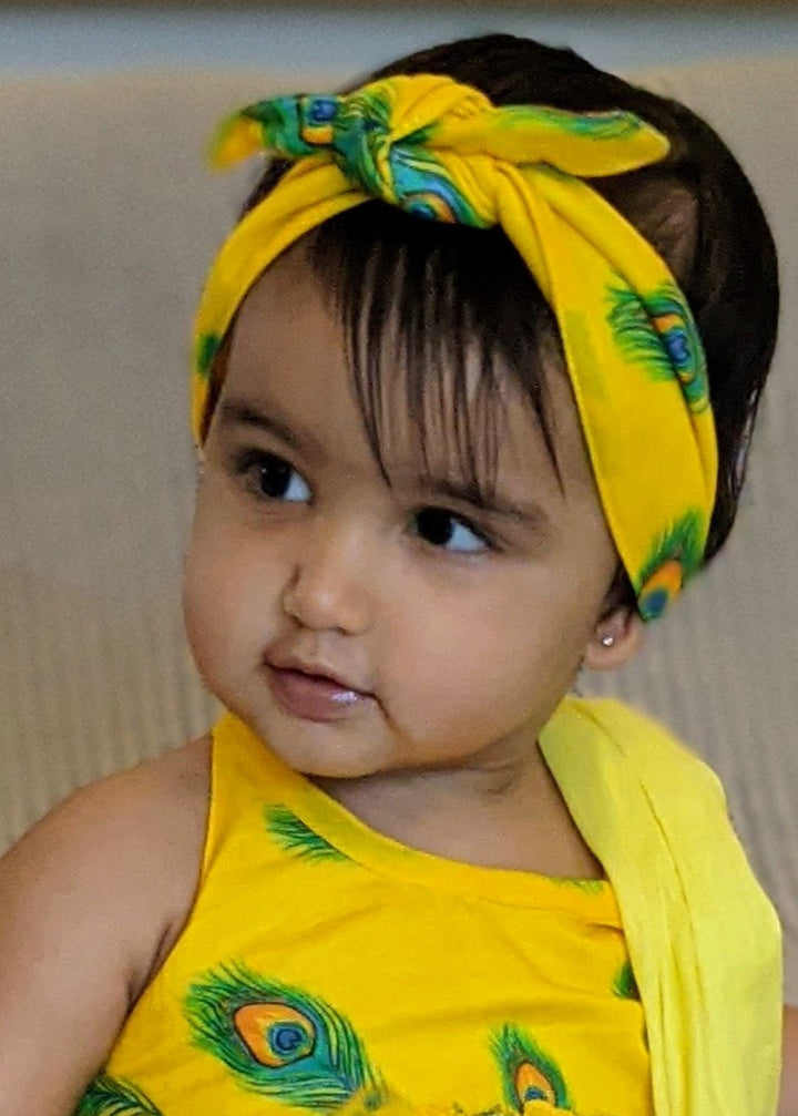 A young child with a yellow hairband featuring a peacock design, tied in a turban style.